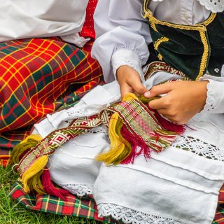 Hands weaving a sash on a Lithuanian national costume