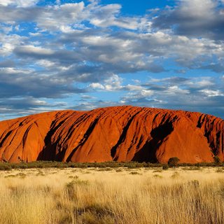 Uluru glowing red beneath a clouded sky